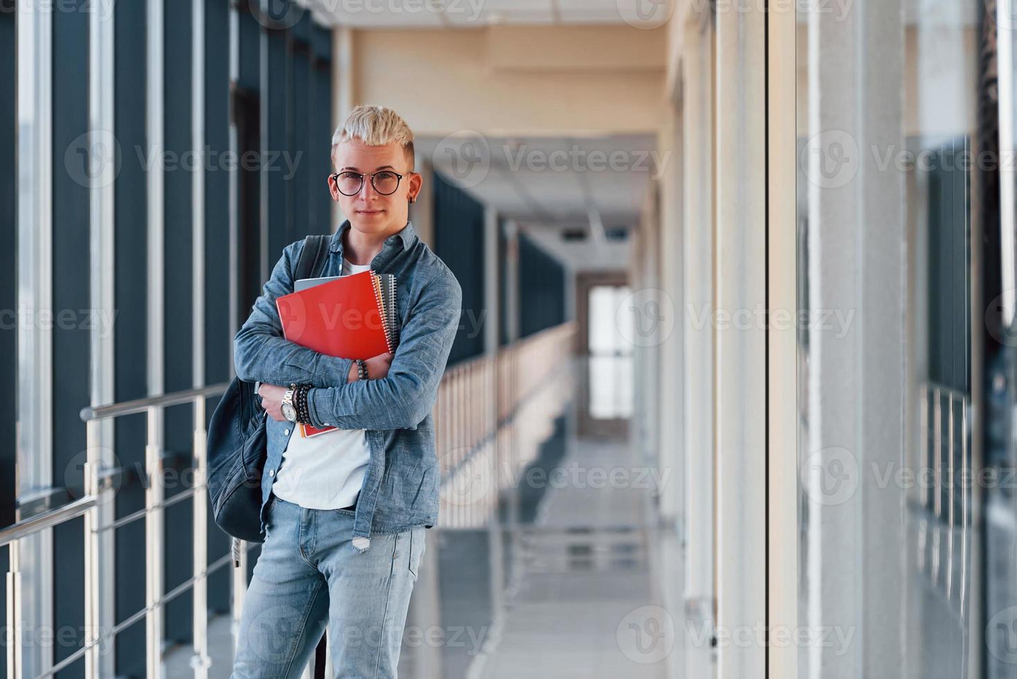 männlicher junger student in jeanskleidung ist im flur eines colleges mit notizblock in den händen foto