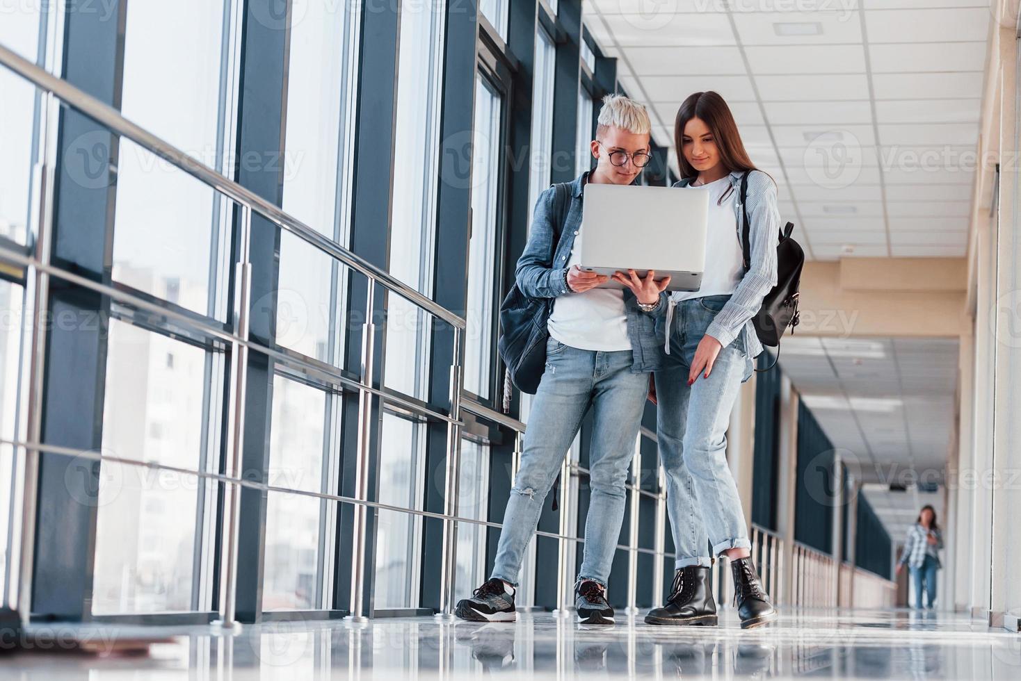 Zwei junge Studentenfreunde zusammen in einem Korridor eines Colleges mit Laptop in den Händen foto