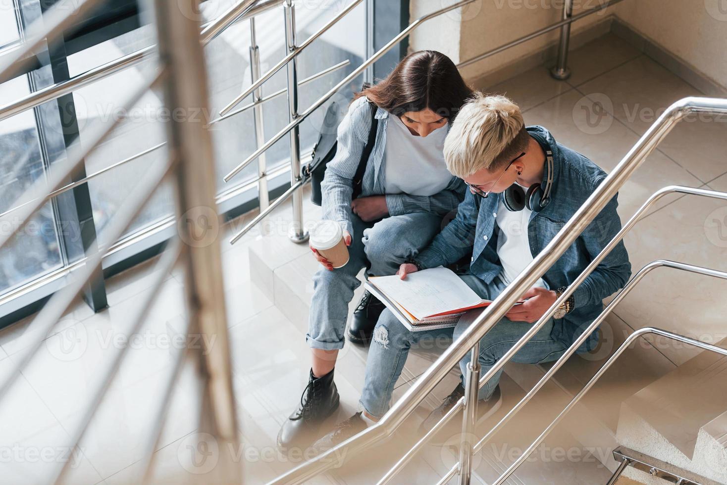 Zwei junge Studentenfreunde sitzen und lesen zusammen Buch auf der Treppe im College foto