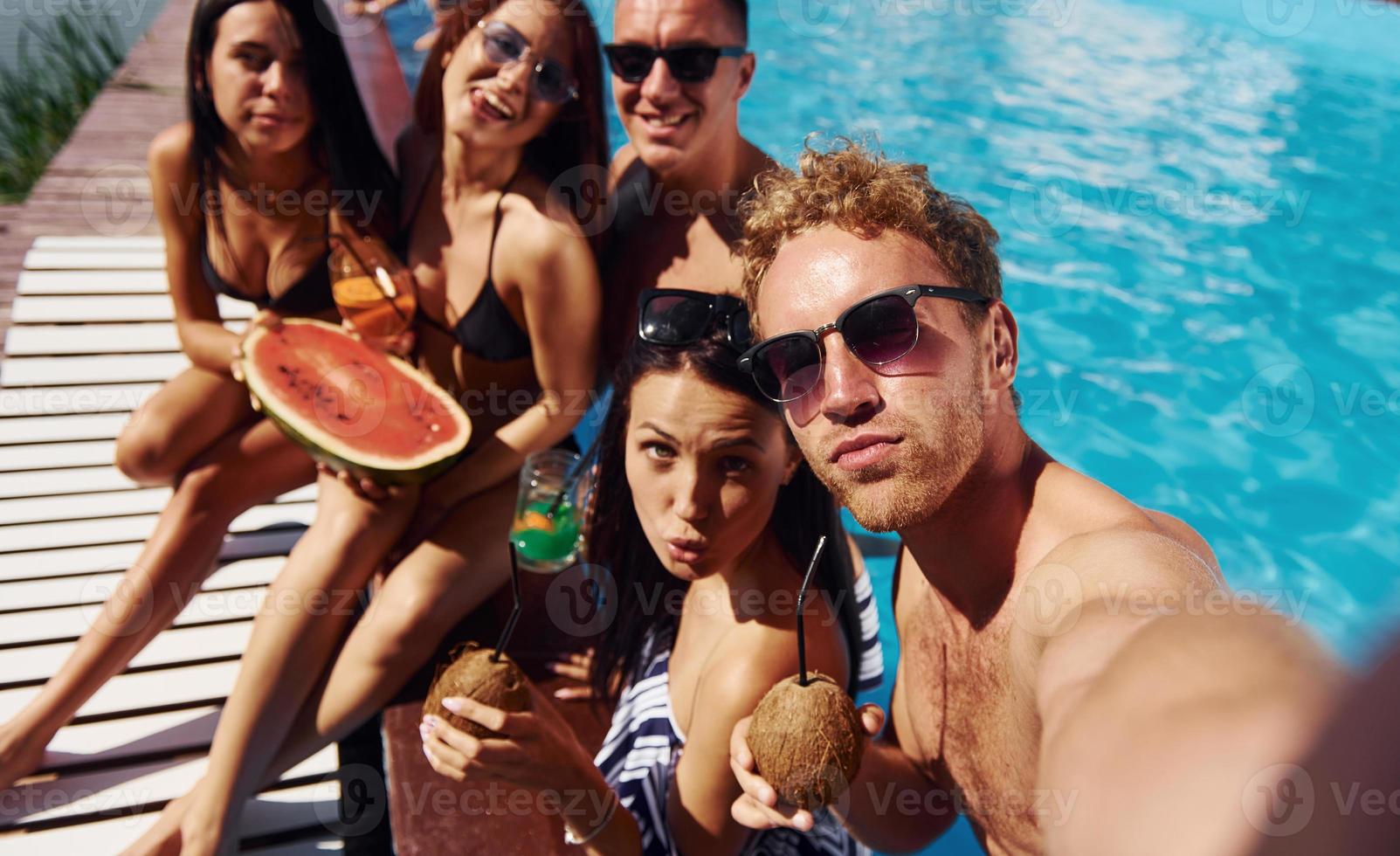 hält Wassermelone. gruppe junger glücklicher leute haben tagsüber spaß im schwimmbad foto