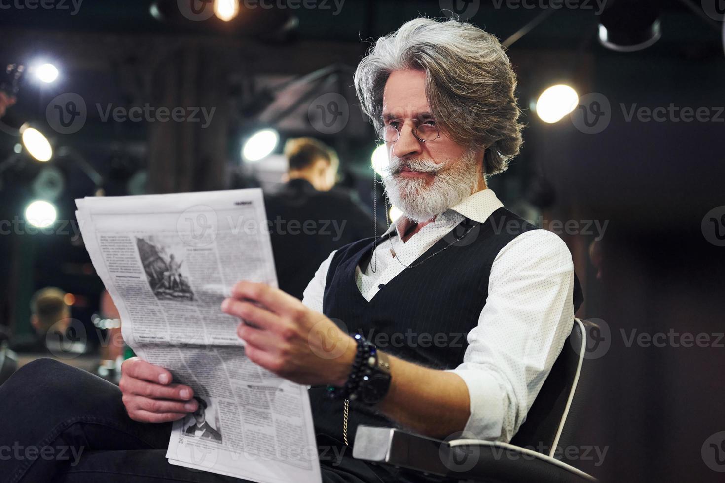 Zeitung lesen. Stilvoller moderner Senior mit grauem Haar und Bart ist drinnen foto