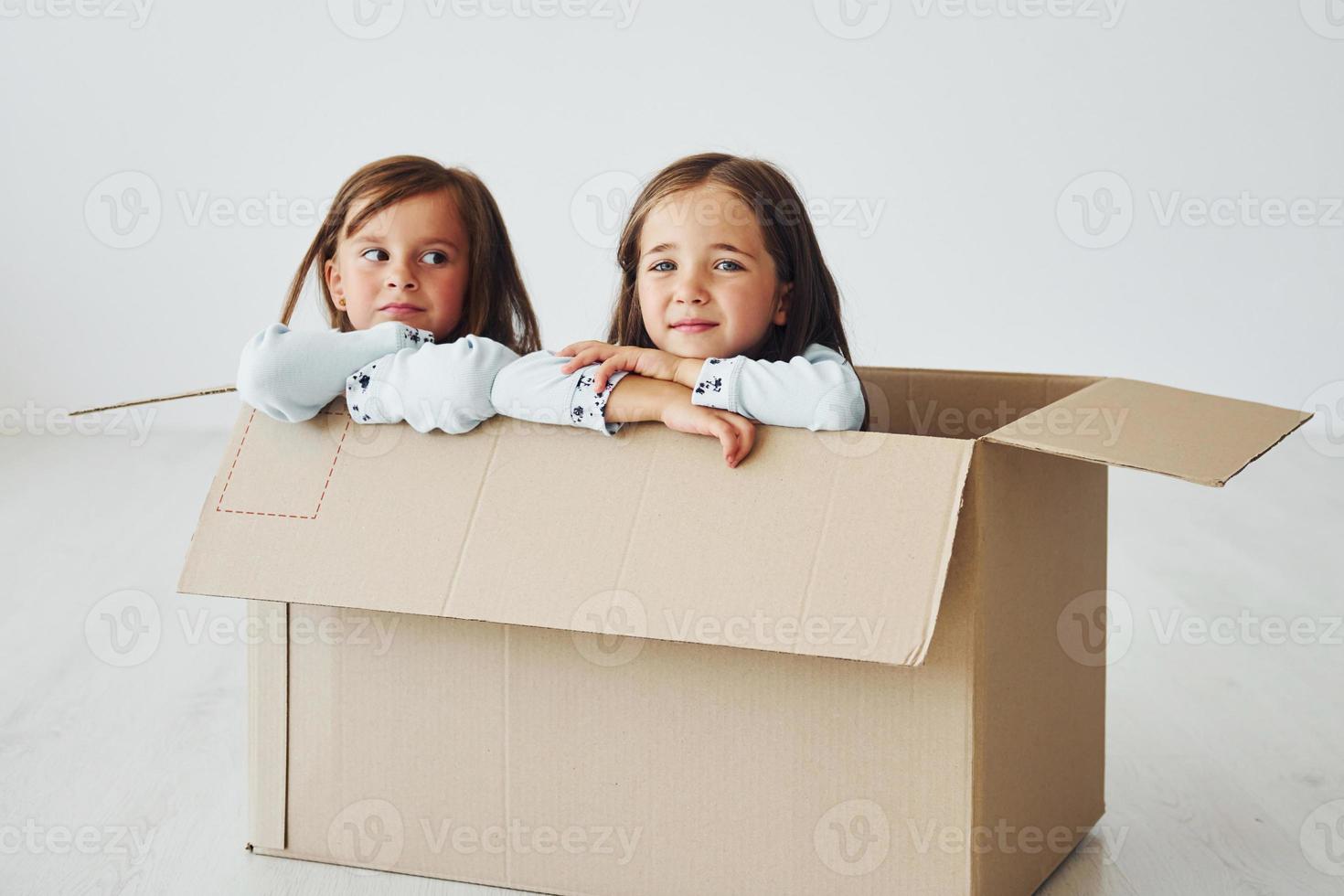 in der Pappschachtel sitzen. Zwei süße kleine Mädchen drinnen zu Hause zusammen. Kinder haben Spaß foto