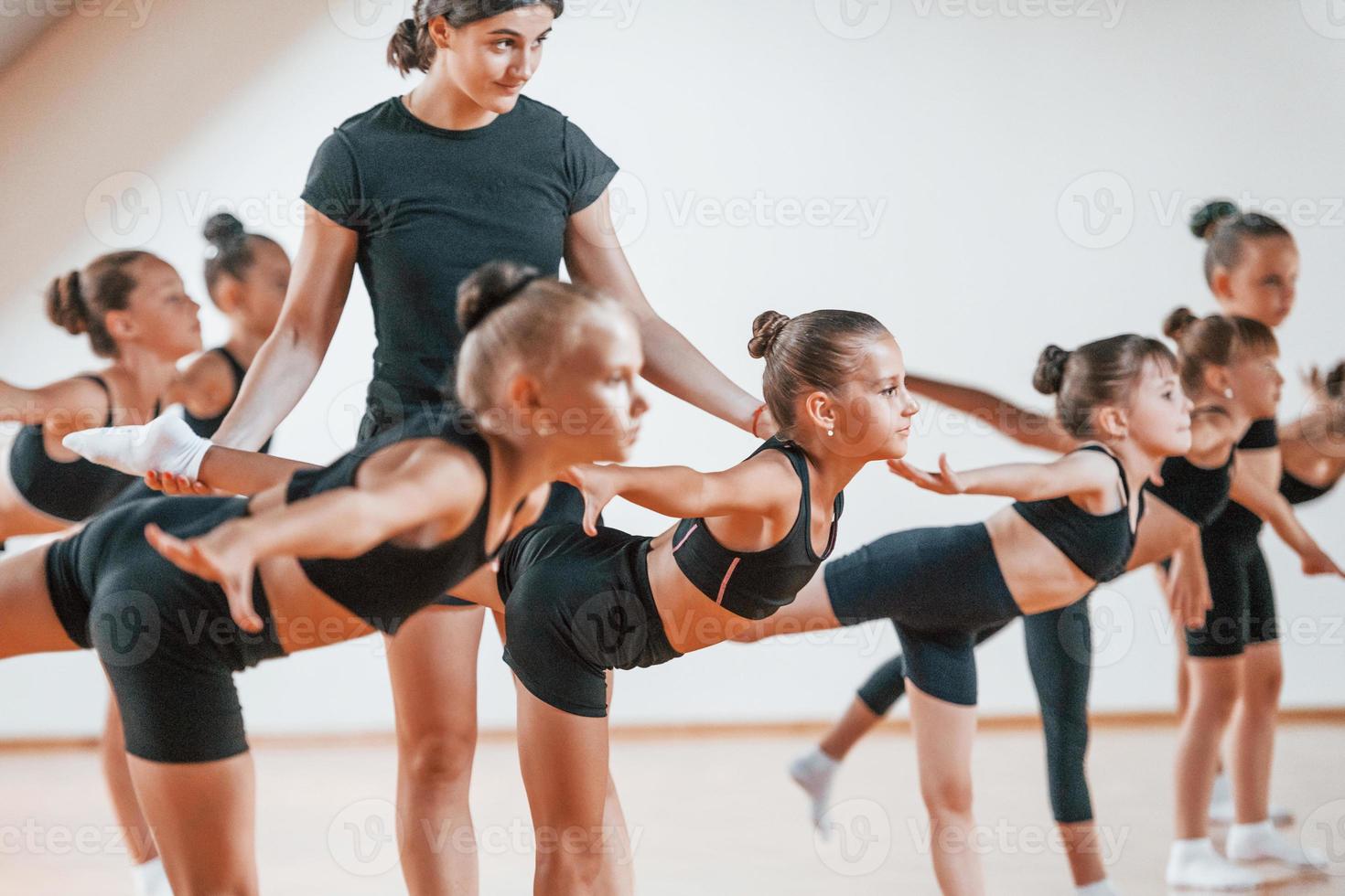 Trainer hilft. Gruppe weiblicher Kinder, die gemeinsam Sportübungen im Innenbereich praktizieren foto