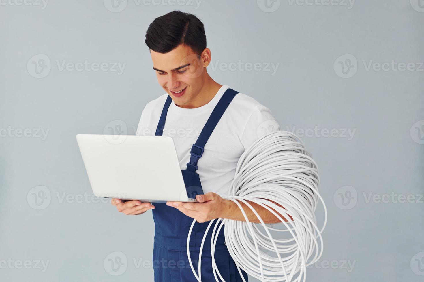 nutzt Laptop. männlicher Arbeiter in blauer Uniform, der im Studio vor weißem Hintergrund steht foto