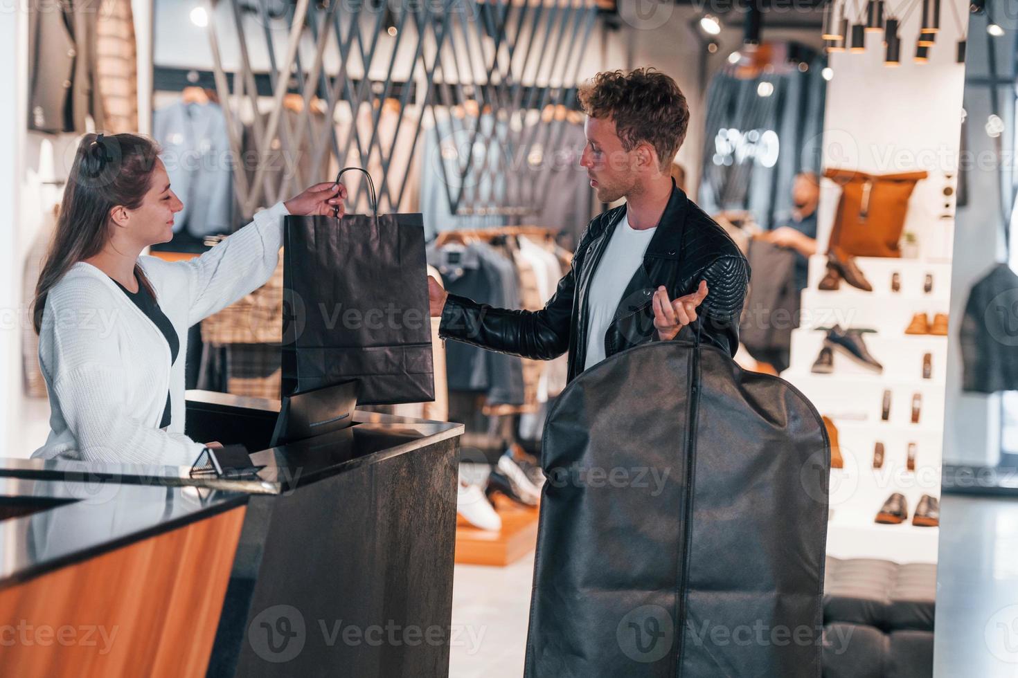 mann kauft in modernem geschäft mit eleganter kleidung ein. Arbeiterin bedient den Mann an der Kasse foto