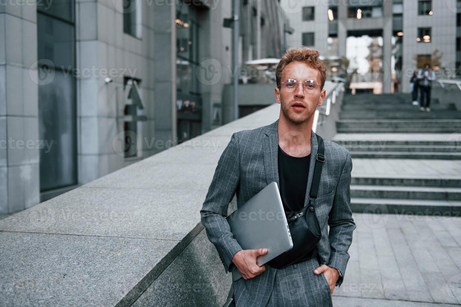 Laptop in den Händen. junger eleganter mann in guter kleidung ist tagsüber draußen in der stadt foto