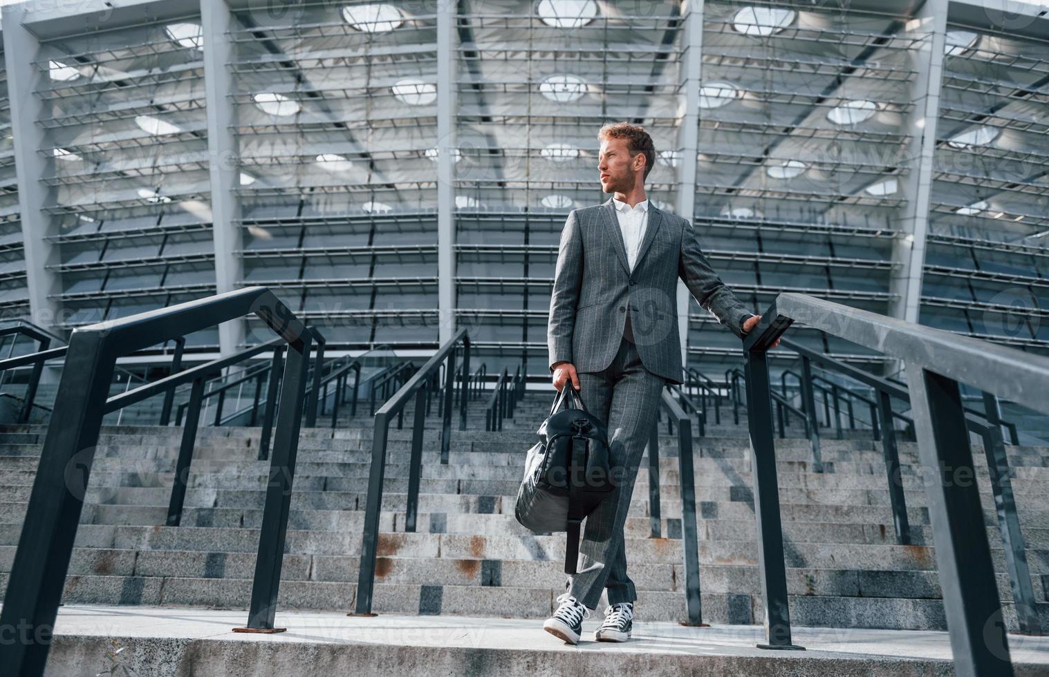 auf der Treppe des Stadions. Junger Geschäftsmann in grauer Abendgarderobe ist draußen in der Stadt foto