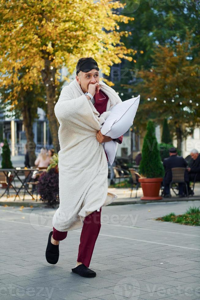 junger mann im pyjama ist draußen auf der straße. fühlt sich schläfrig foto