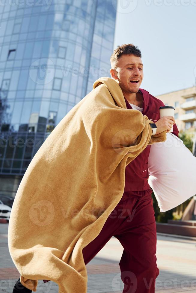 laufen, zu spät zur Arbeit. junger mann im pyjama ist draußen auf der straße. fühlt sich schläfrig foto