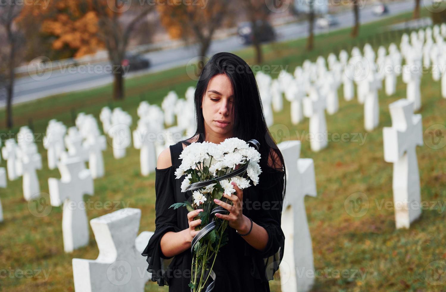 junge Frau in schwarzer Kleidung, die den Friedhof mit vielen weißen Kreuzen besucht. Vorstellung von Begräbnis und Tod foto