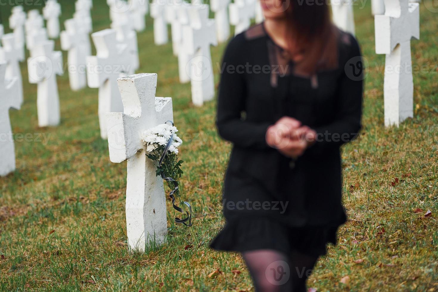 gibt Respekt, indem er Blumen legt. junge Frau in schwarzer Kleidung, die den Friedhof mit vielen weißen Kreuzen besucht. Vorstellung von Begräbnis und Tod foto