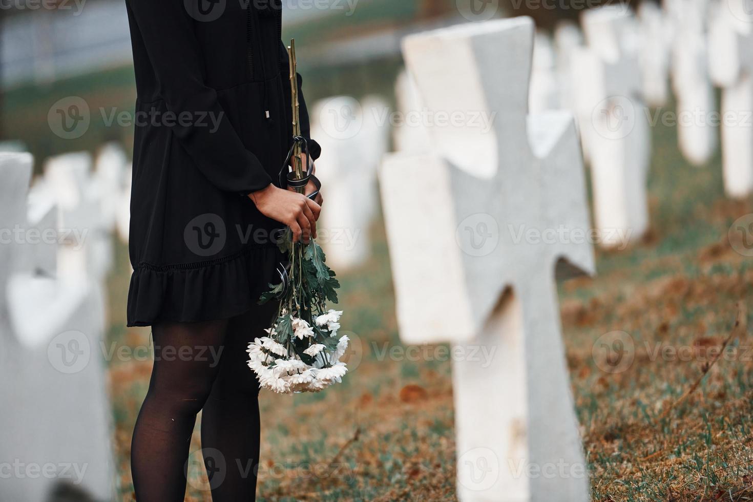 Partikelansicht. junge Frau in schwarzer Kleidung, die den Friedhof mit vielen weißen Kreuzen besucht. Vorstellung von Begräbnis und Tod foto