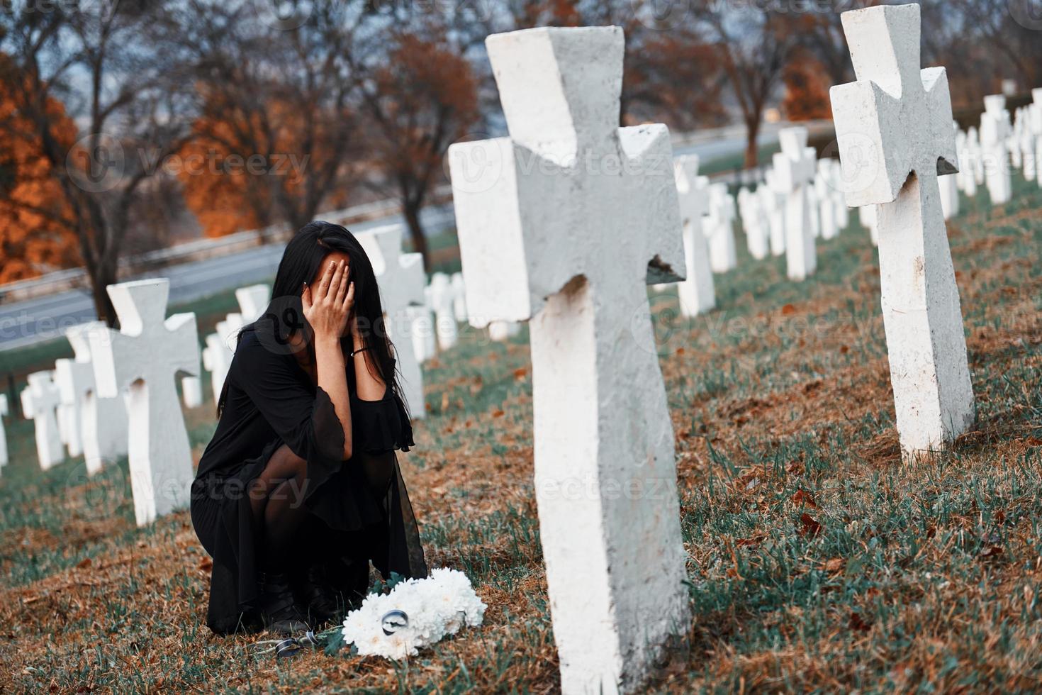 mit Blumen in den Händen. junge Frau in schwarzer Kleidung, die den Friedhof mit vielen weißen Kreuzen besucht. Vorstellung von Begräbnis und Tod foto