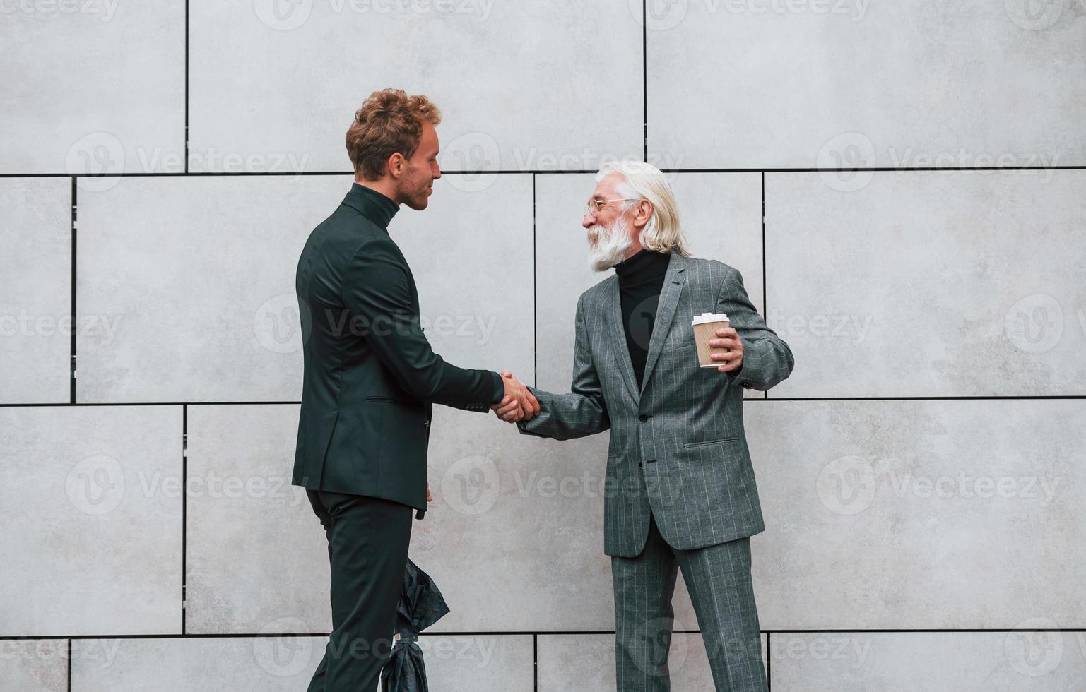 Regenschirm und Tasse Getränk. junger mann mit senior in eleganter kleidung ist zusammen im freien. Geschäftskonzept foto