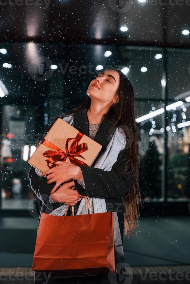 aus dem Shop mit Geschenkbox in den Händen. Fröhliche Frau ist in den Weihnachtsferien im Freien. Konzeption des neuen Jahres foto