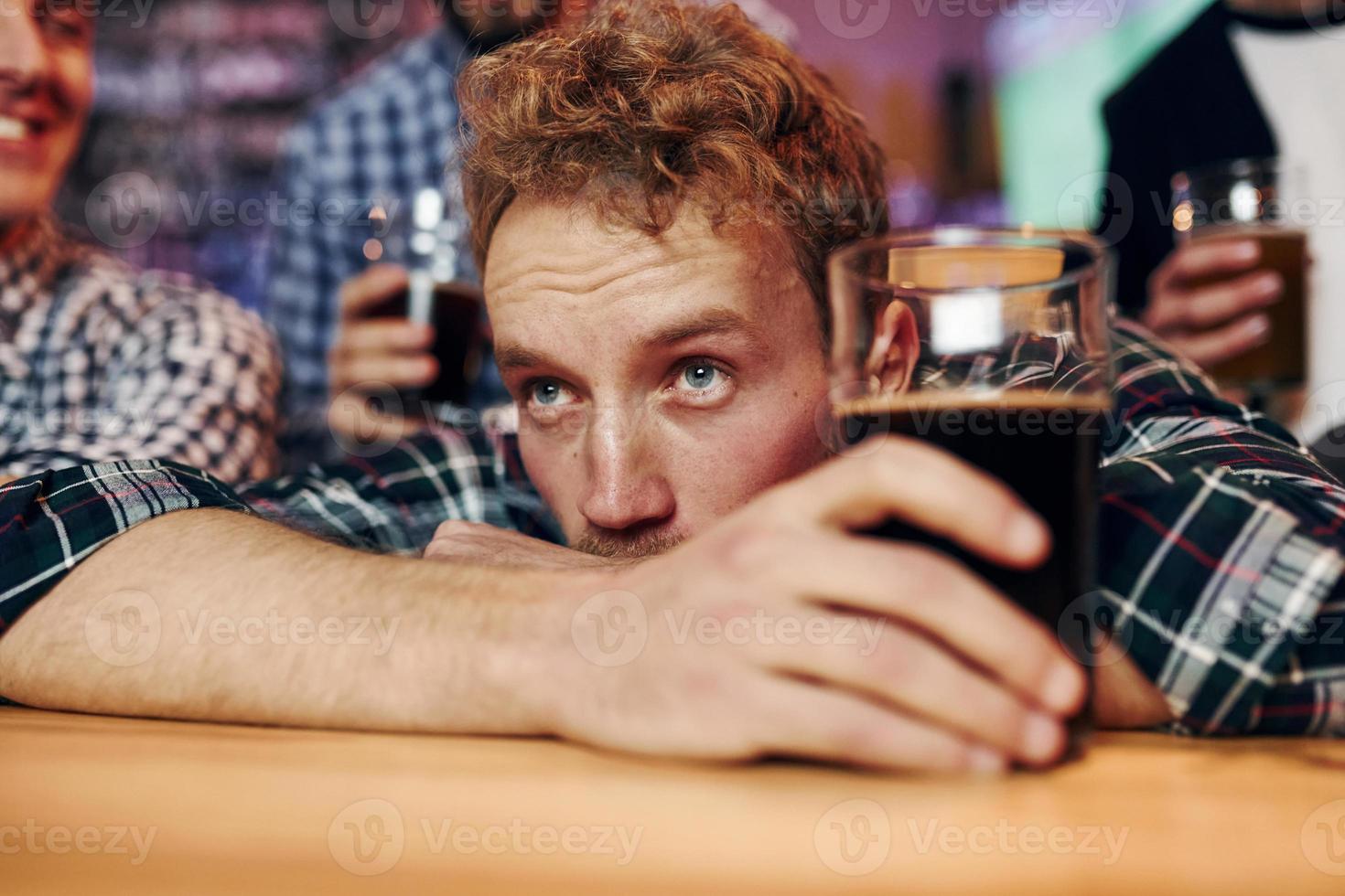 Trauriger Mann fühlt sich schlecht. gruppe von menschen zusammen drinnen in der kneipe haben spaß am wochenende foto