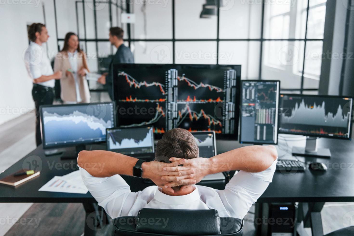 mann sitzt auf stuhl und macht pause. Das Team von Börsenmaklern arbeitet in einem modernen Büro mit vielen Bildschirmen foto