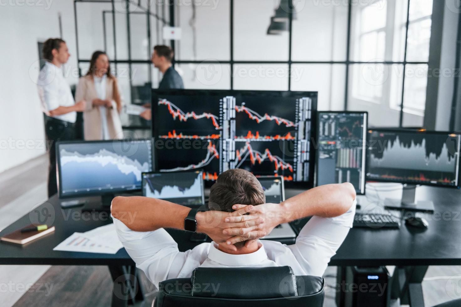 mann sitzt auf stuhl und macht pause. Das Team von Börsenmaklern arbeitet in einem modernen Büro mit vielen Bildschirmen foto