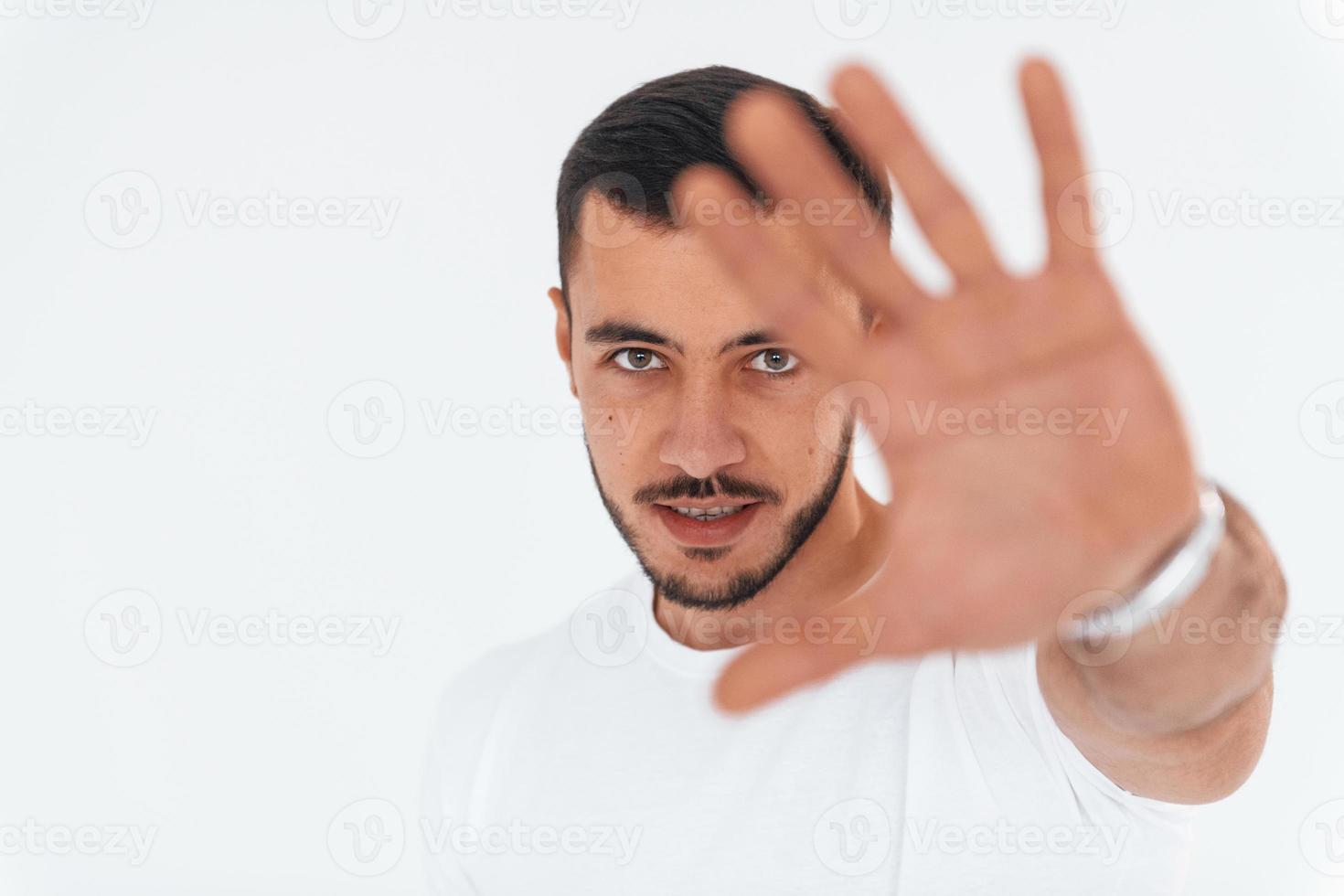 Geste stoppen. junger gutaussehender Mann, der drinnen vor weißem Hintergrund steht foto