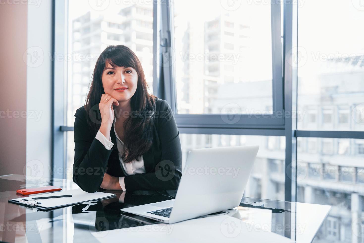 mit Laptop auf dem Tisch. Frau in schwarzer formeller Kleidung ist drinnen im modernen Büro foto