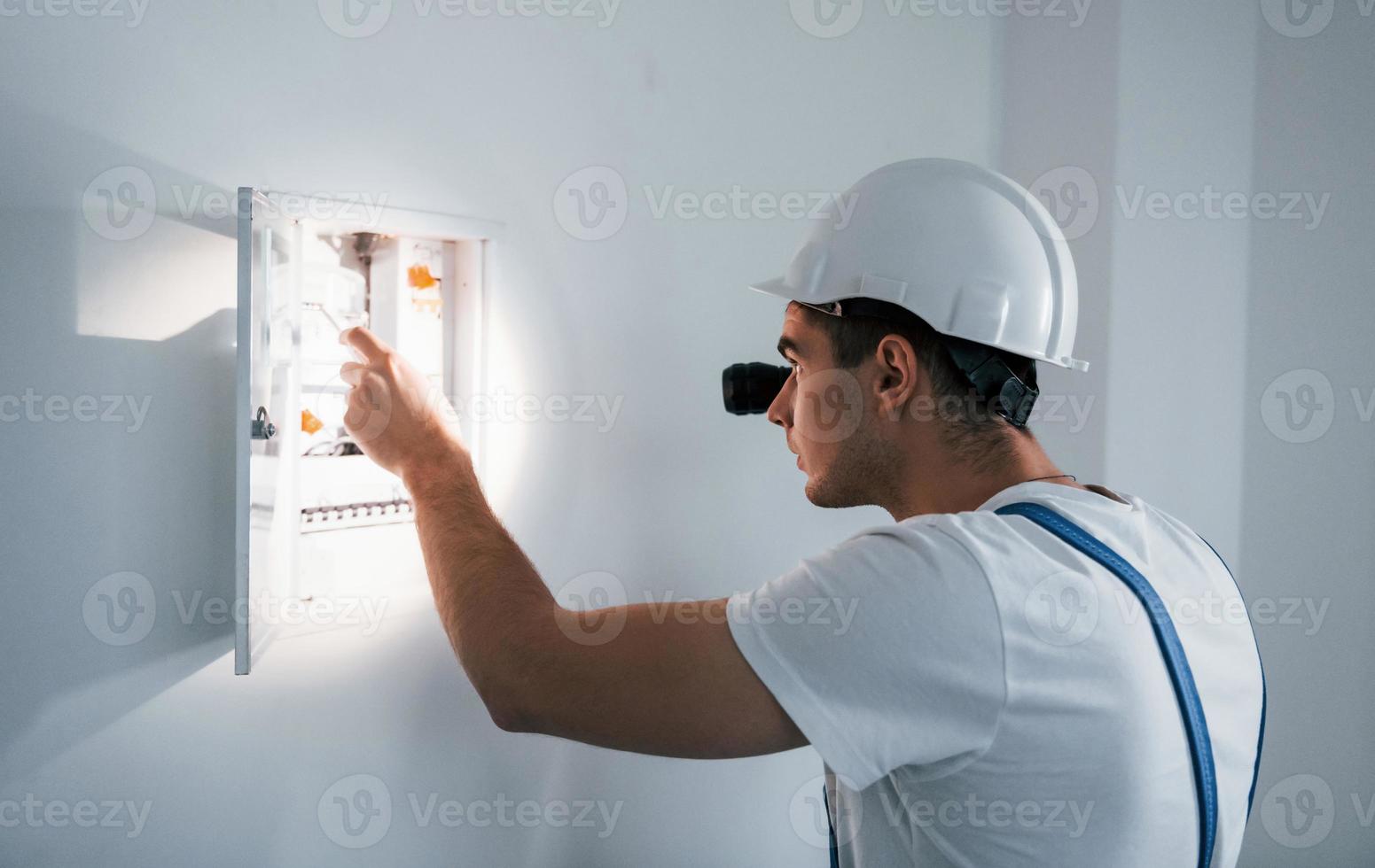 junger männlicher elektriker mit weißem schutzhelm arbeitet drinnen im raum foto
