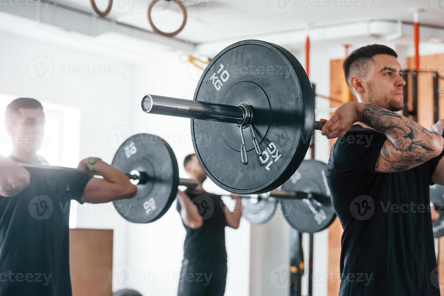 durch den Einsatz schwerer Gewichte. eine gruppe junger sportlicher leute hat drinnen im fitnessstudio einen crossfit-tag foto