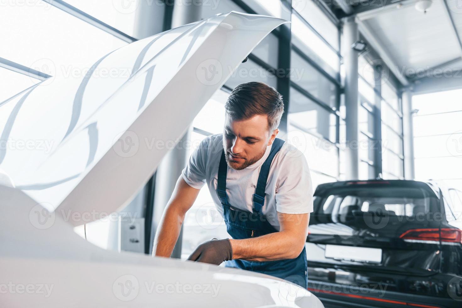 Qualitätsdienstleistung; Qualitätsservice. junger mann in weißem hemd und blauer uniform repariert autos foto