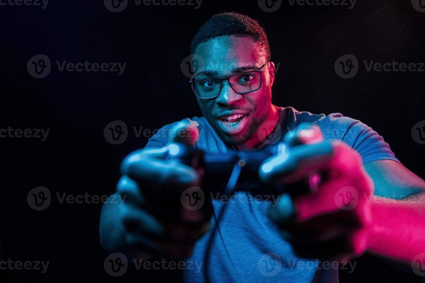 spielt Spiel mit Controller. futuristische neonbeleuchtung. junger Afroamerikaner im Studio foto