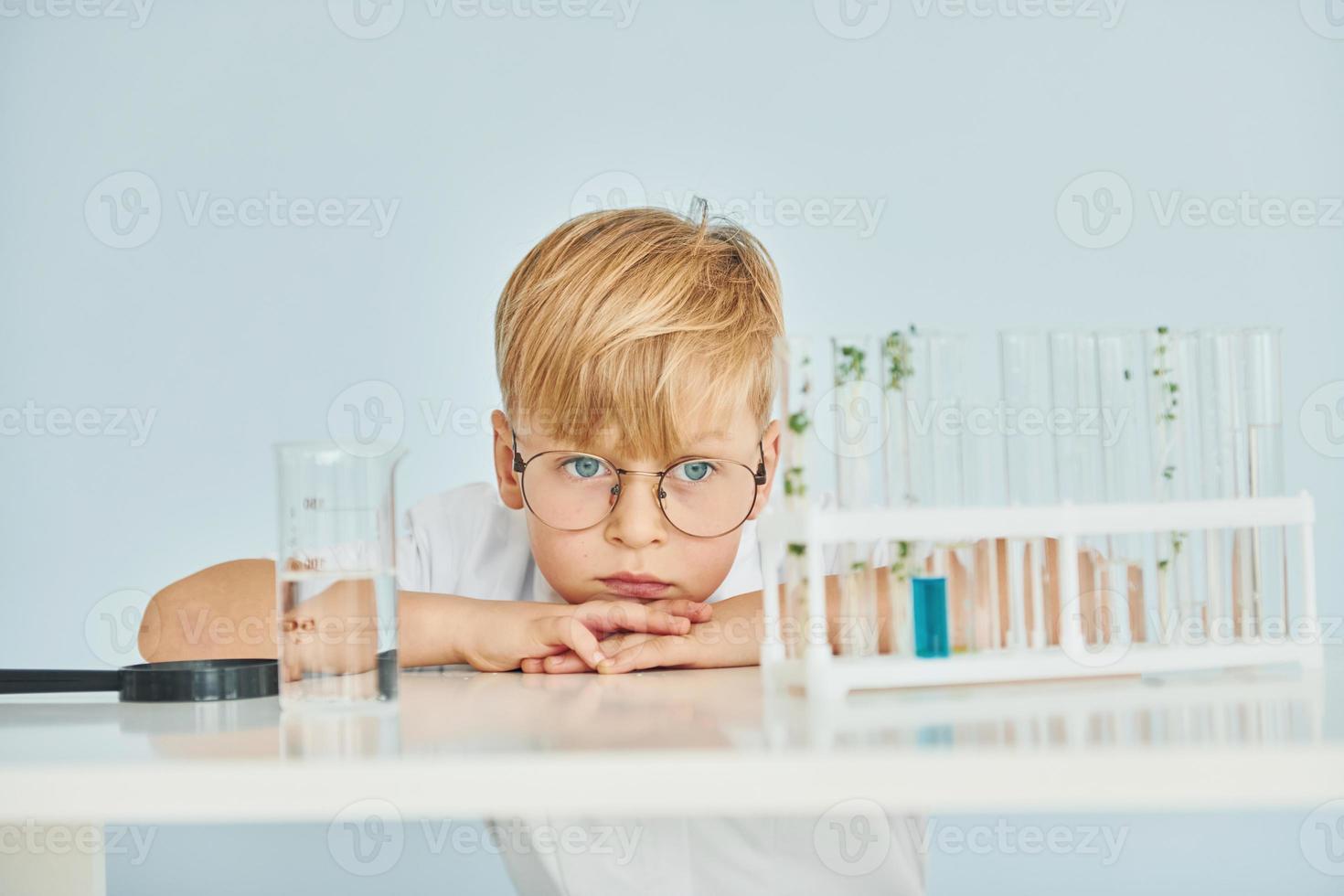 verwendet Reagenzgläser. kleiner junge im mantel, der einen wissenschaftler im labor spielt, indem er ausrüstung verwendet foto