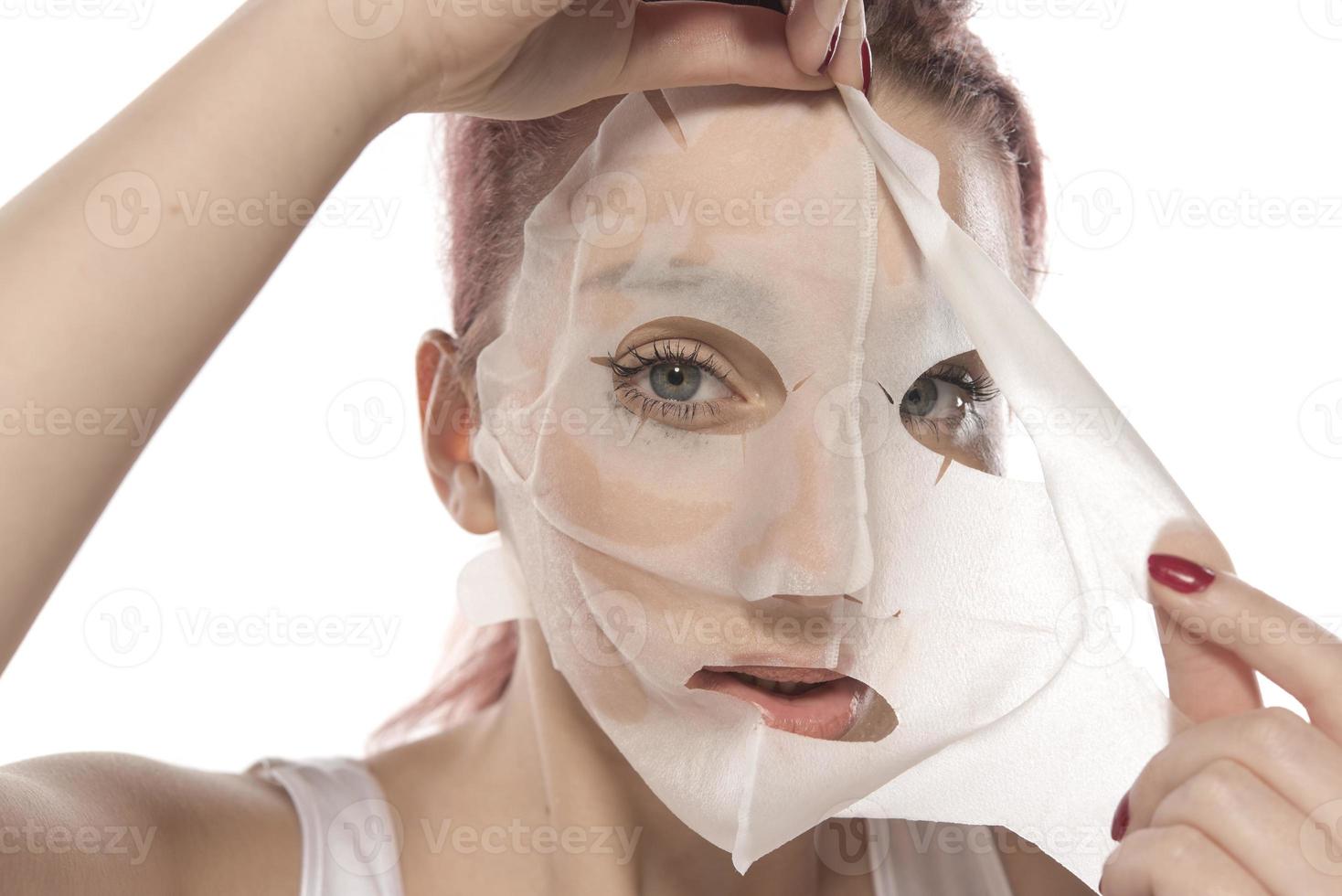 Gesichtspflege und Schönheitsbehandlungen. Frau mit einer feuchtigkeitsspendenden Blattmaske auf ihrem Gesicht isoliert auf weißem Hintergrund foto