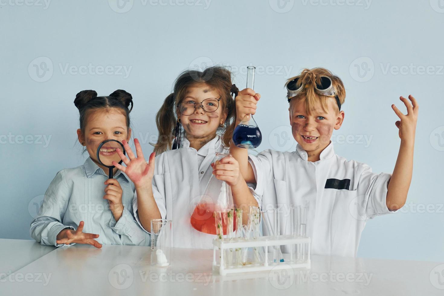 glückliche Freunde lächeln. Kinder in weißen Mänteln spielen einen Wissenschaftler im Labor, indem sie Geräte verwenden foto