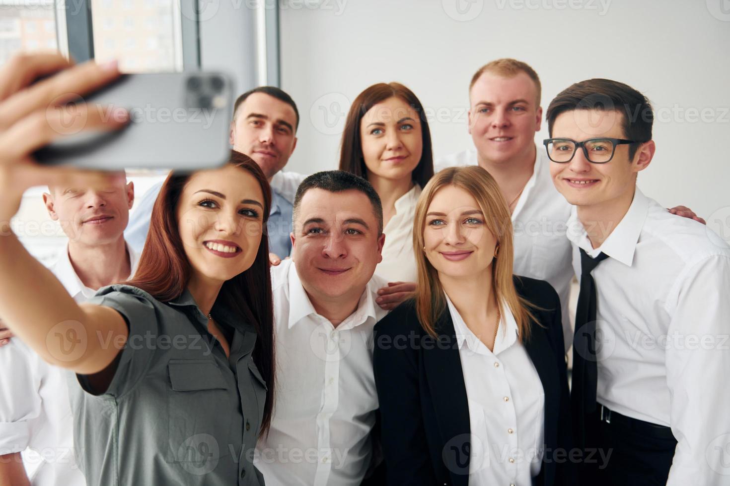 macht Selfie. Gruppe von Personen in offizieller formeller Kleidung, die sich drinnen im Büro befindet foto