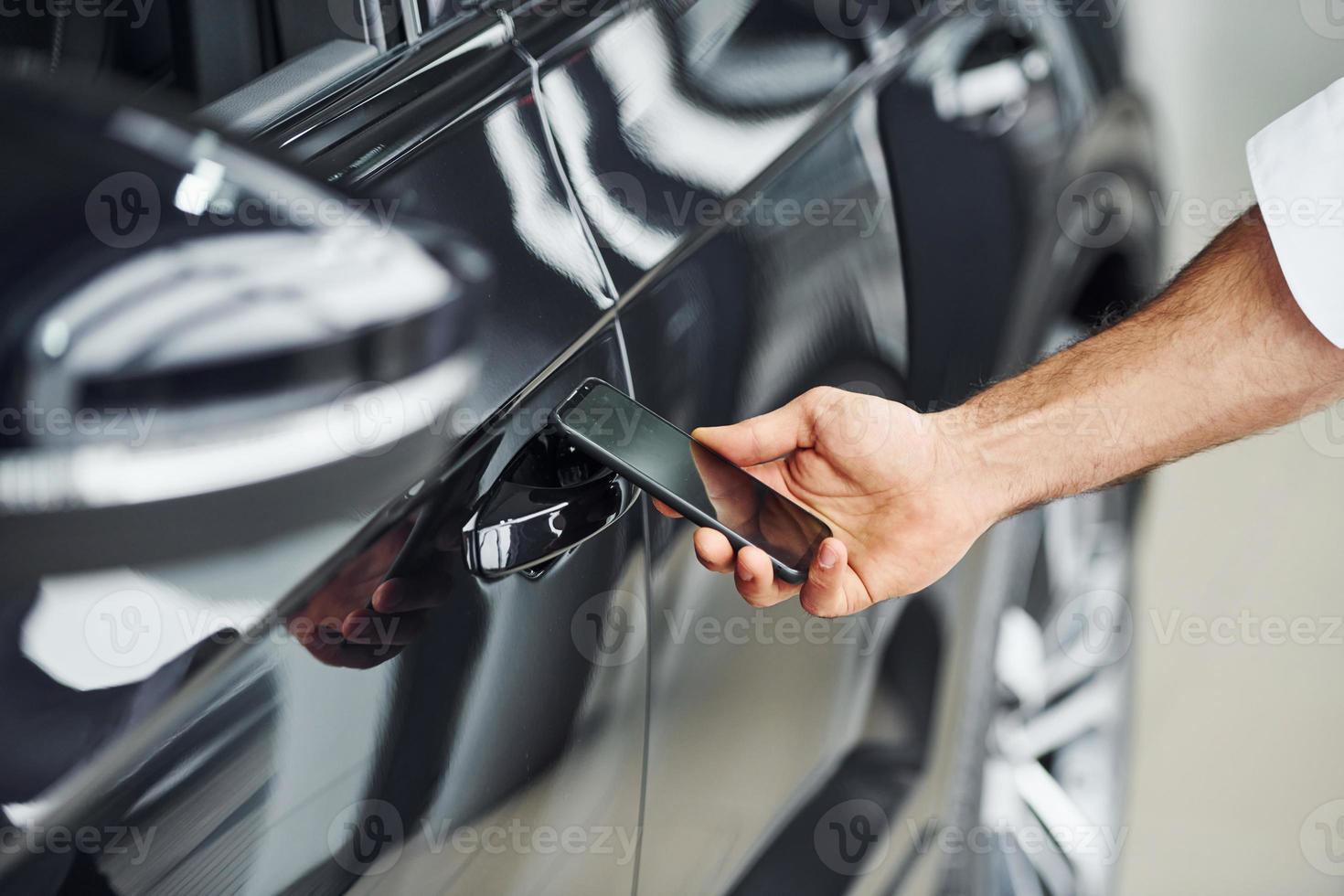 schwarzes Auto. Nahaufnahme der Hand des Mannes, die Telefon mit Etiketten und Symbolen hält. Konzeption der Fernbedienung foto