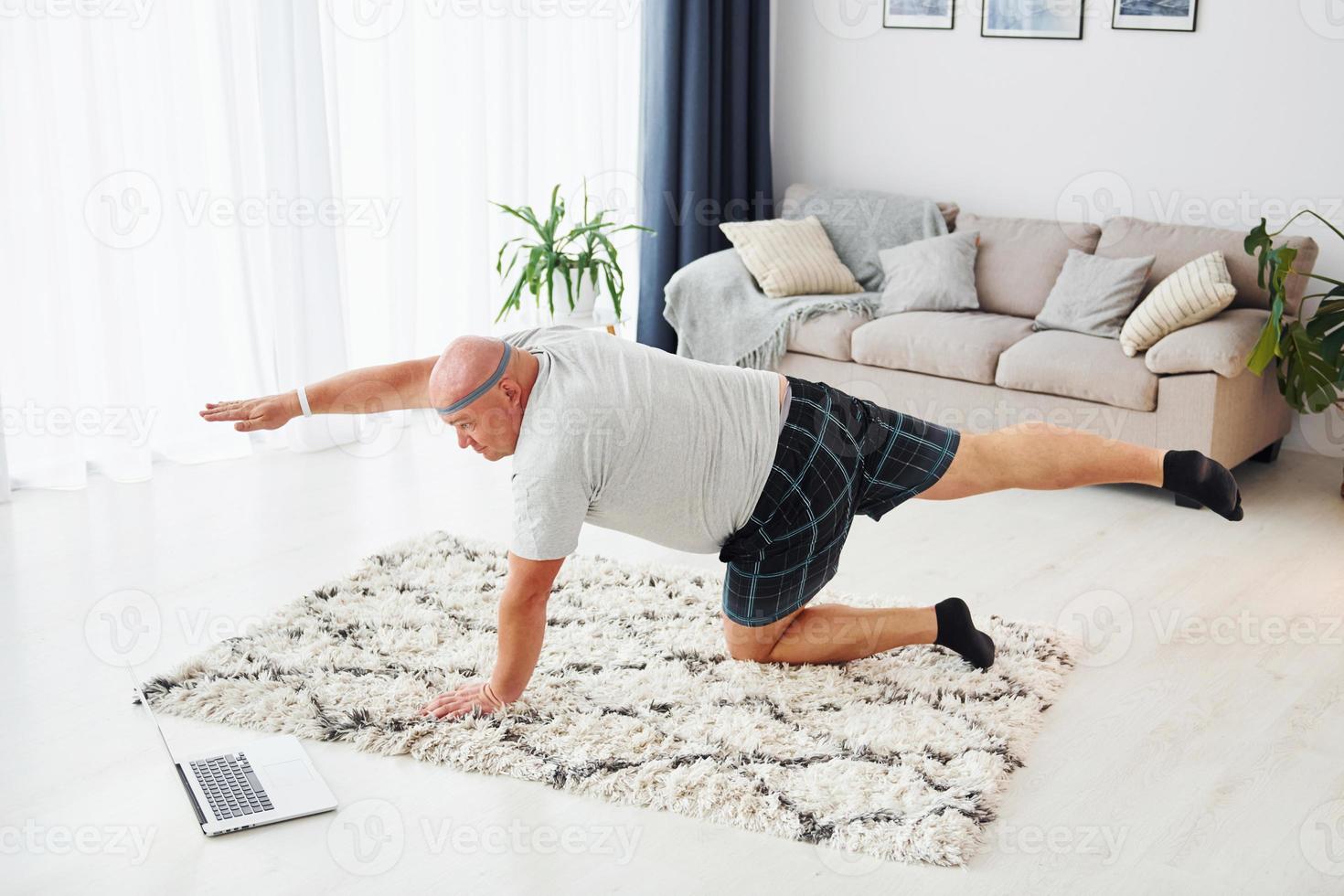 Yogaübungen machen. lustiger übergewichtiger mann in lässiger kleidung ist drinnen zu hause foto