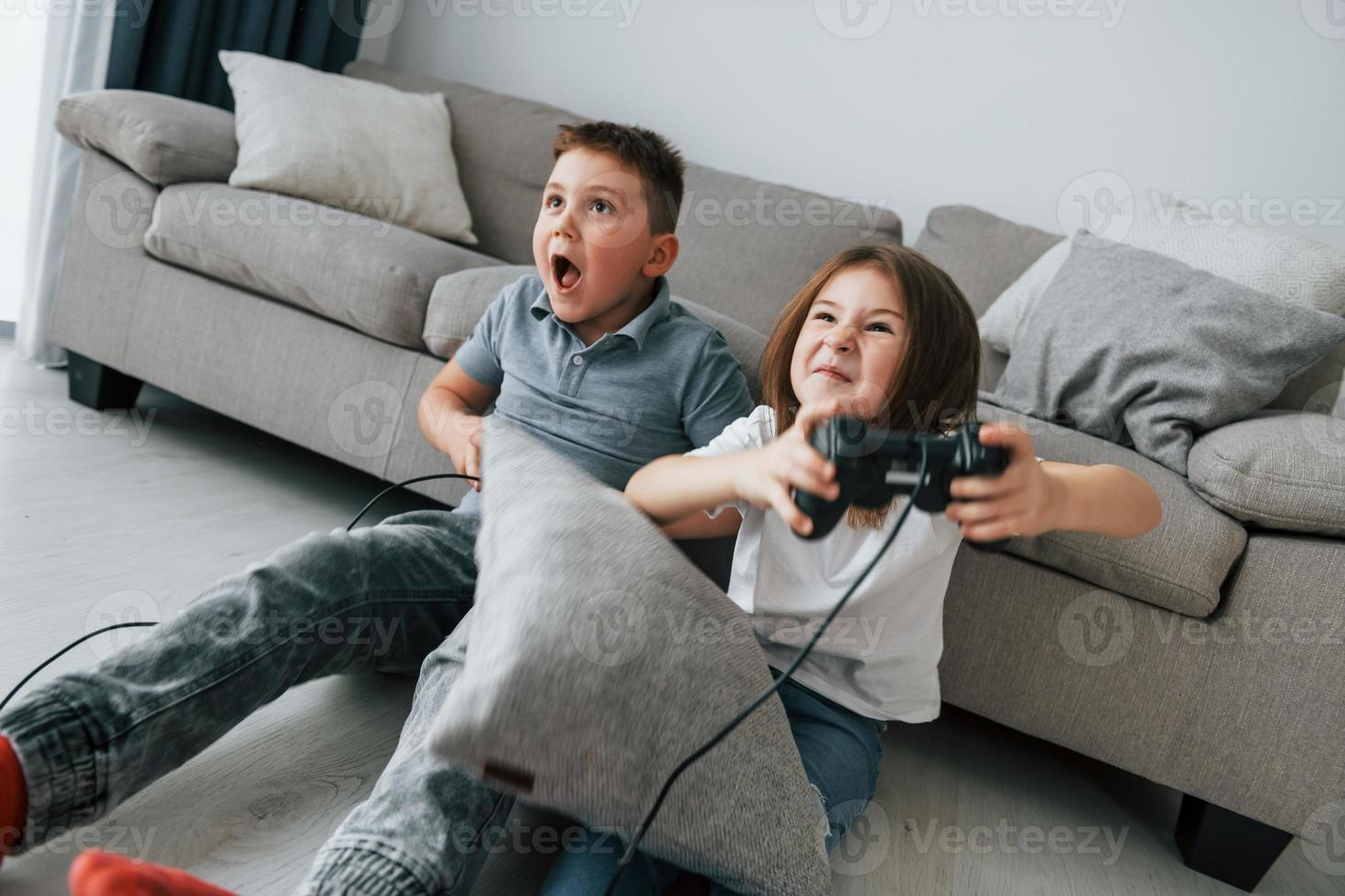 Videospiele spielen. Kinder, die sich tagsüber gemeinsam im Wohnzimmer amüsieren foto