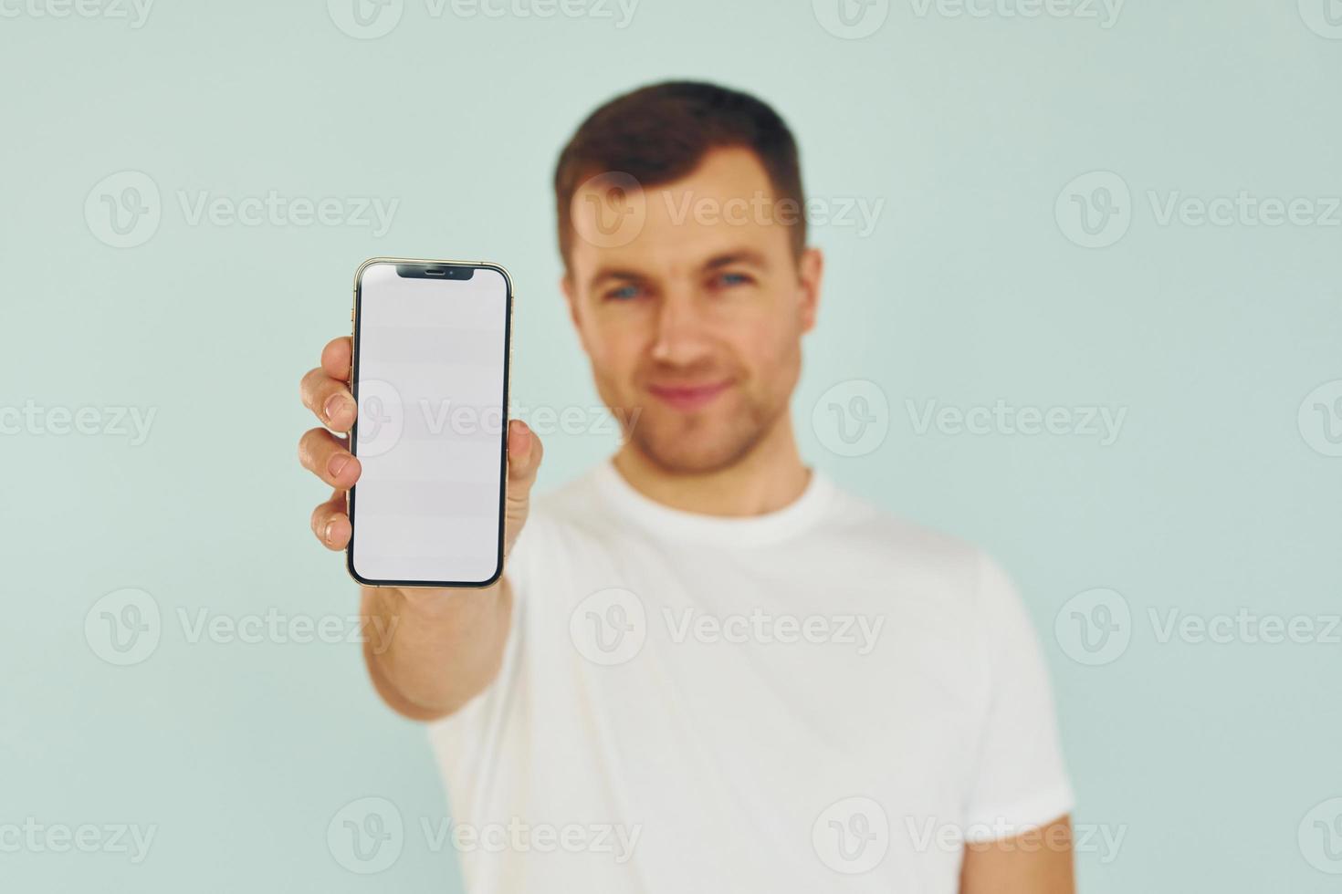Mann in Freizeitkleidung steht im Studio mit Telefon in den Händen foto