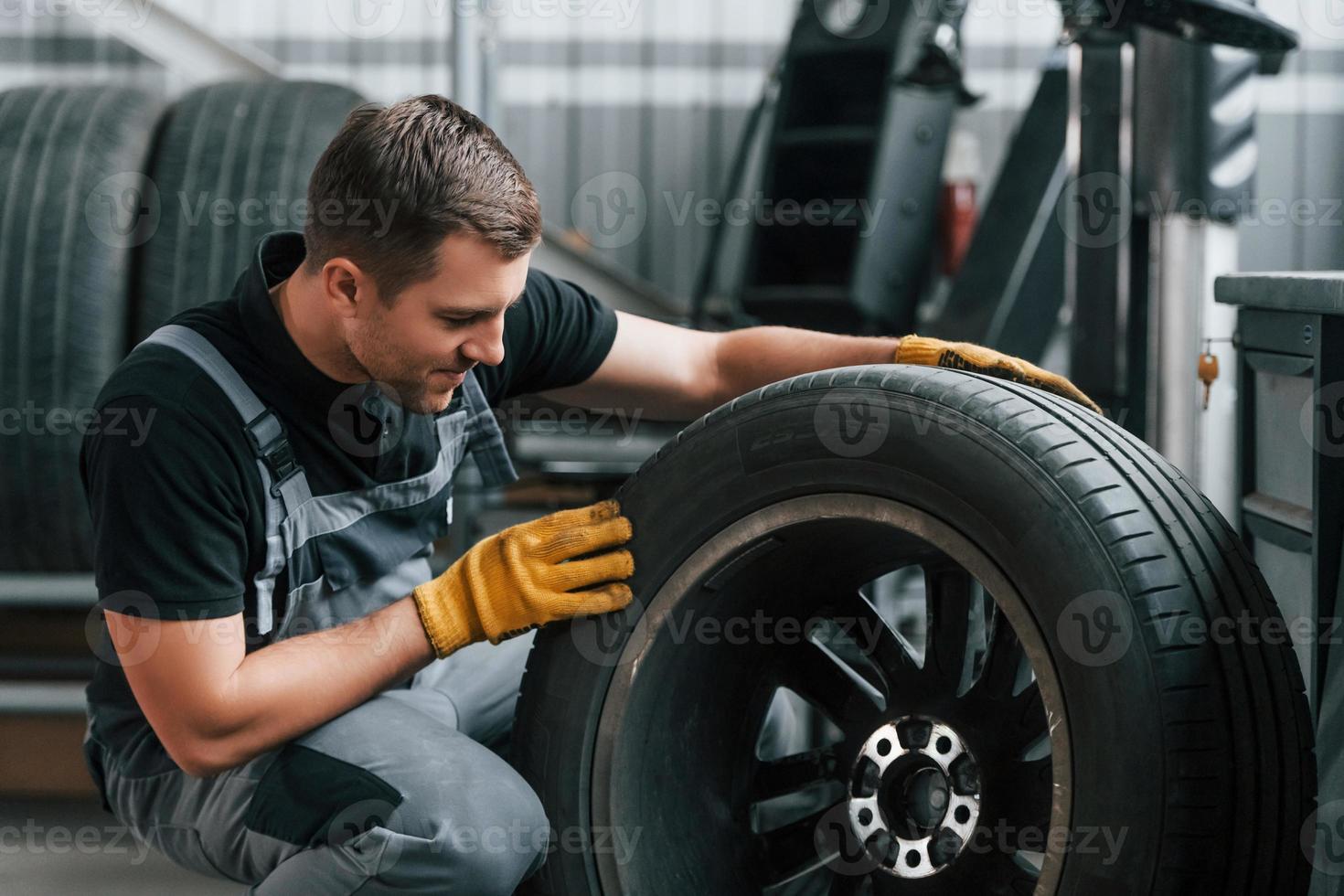 Austausch des alten Reifens. Mann in Uniform arbeitet im Autoservice foto