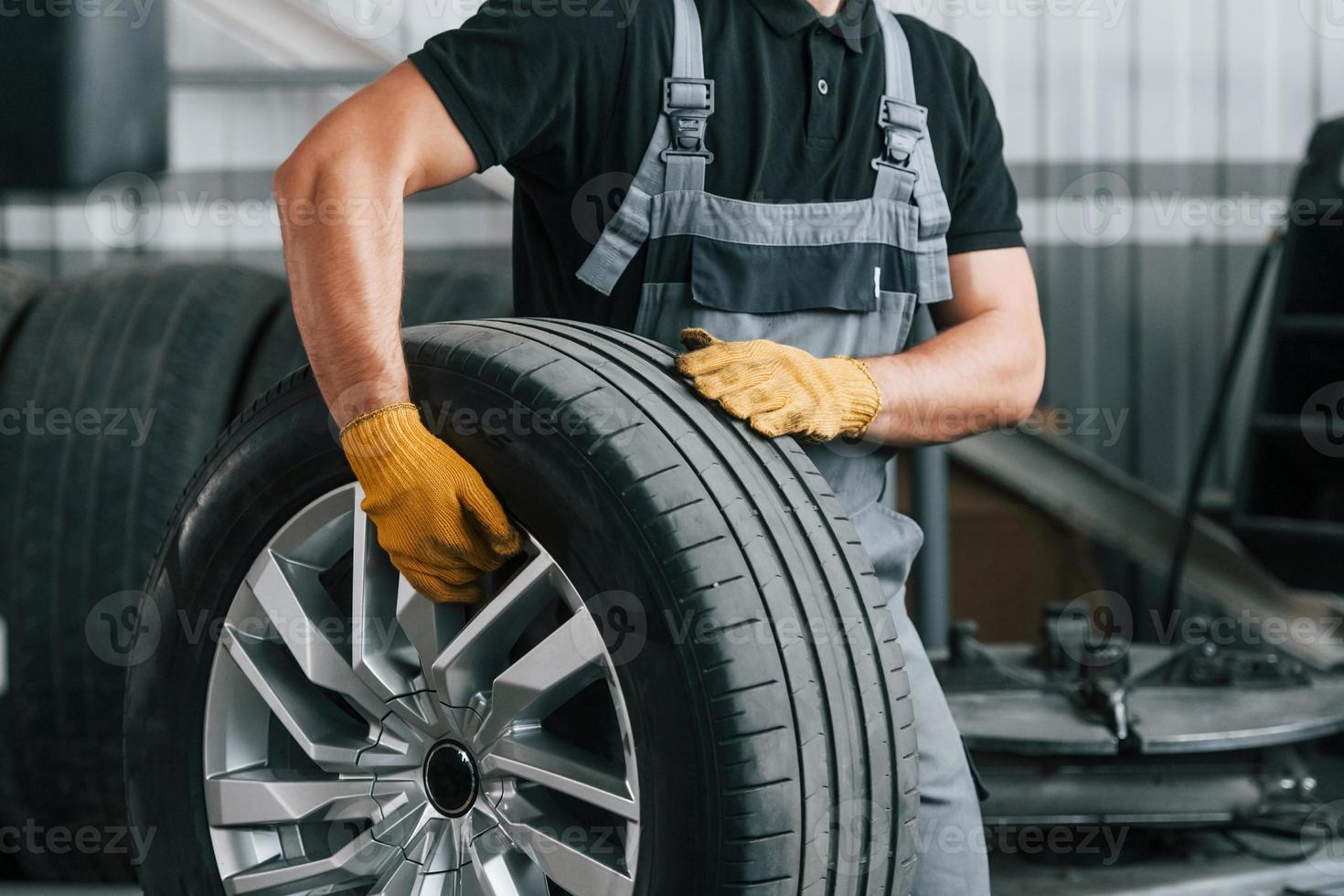 Gehen und Reifen halten. Mann in Uniform arbeitet im Autoservice foto