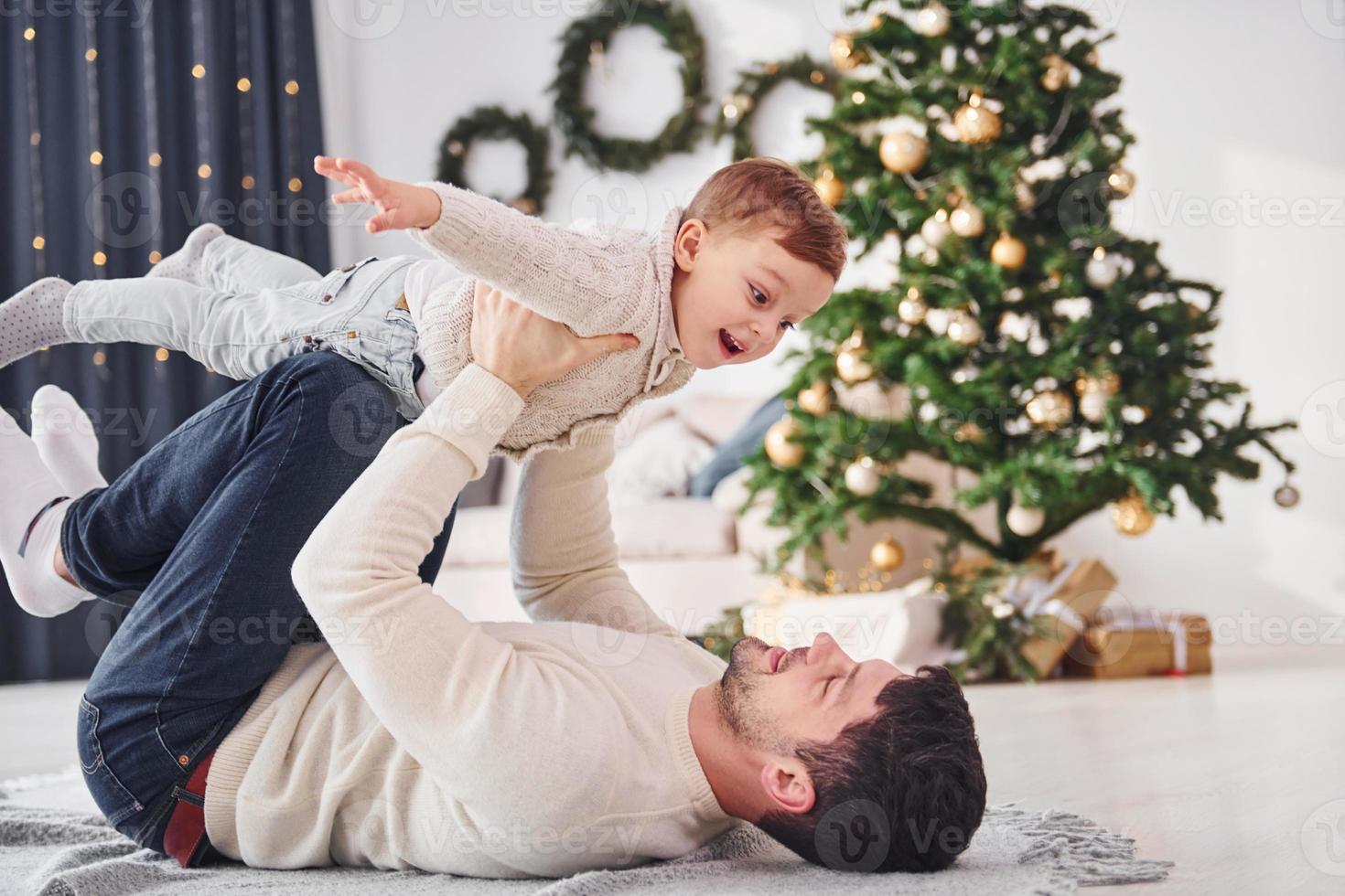 Vater hat Spaß mit seinem Sohn drinnen im weihnachtlich dekorierten Wohnraum foto