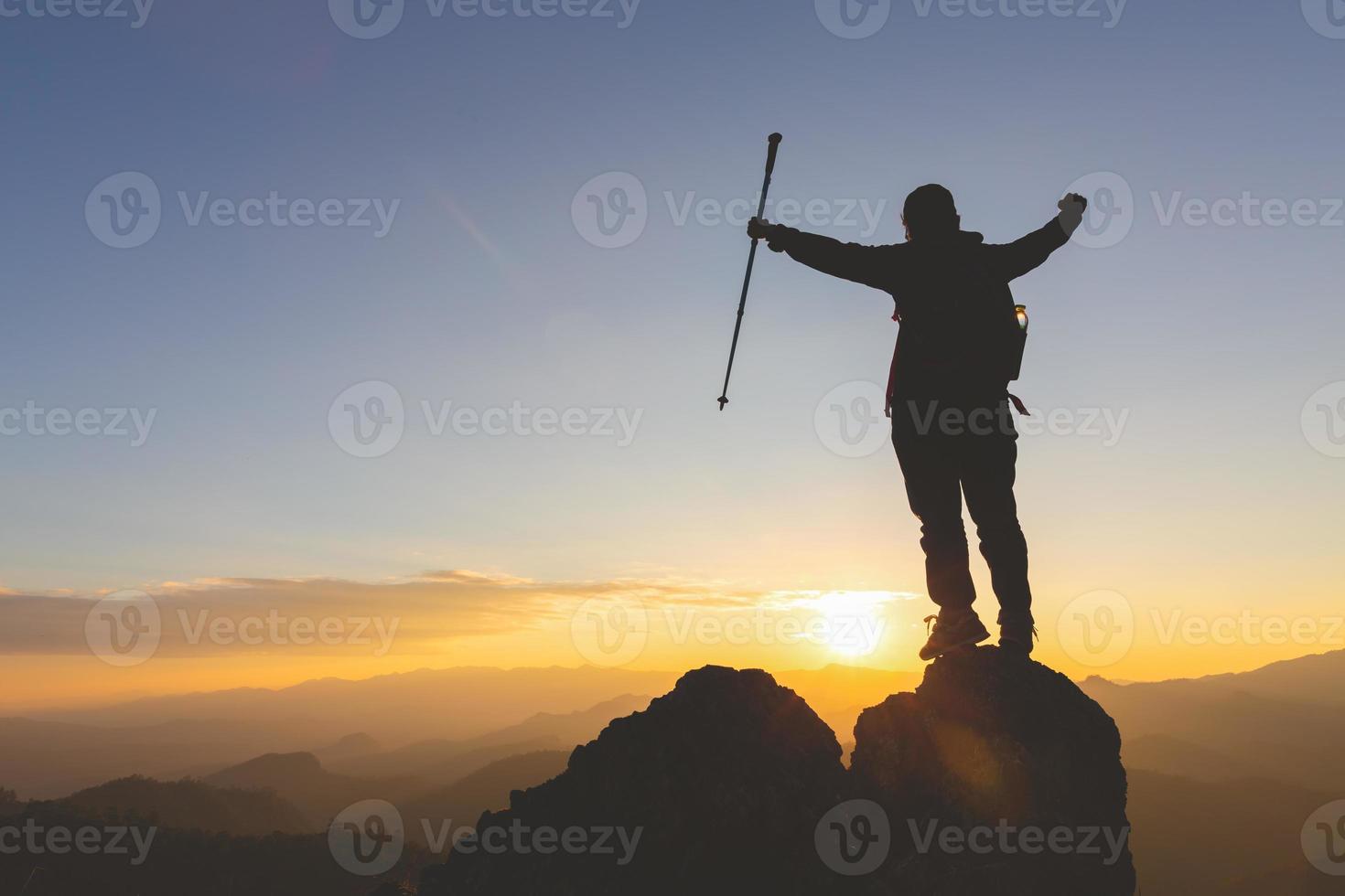 Die Silhouette einer jungen Frau, die allein auf dem Gipfel eines Berges steht und beide Arme hebt, betet und die Natur genießt, zeigt Hoffnung und Freiheit, Erfolg. foto