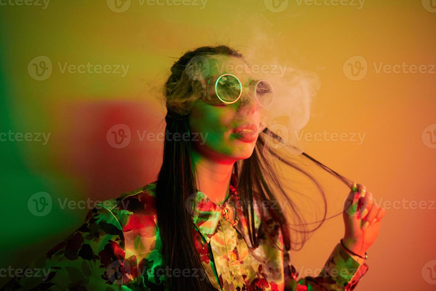 Rauchen, Aktivität. modische junge frau, die im studio mit neonlicht steht foto