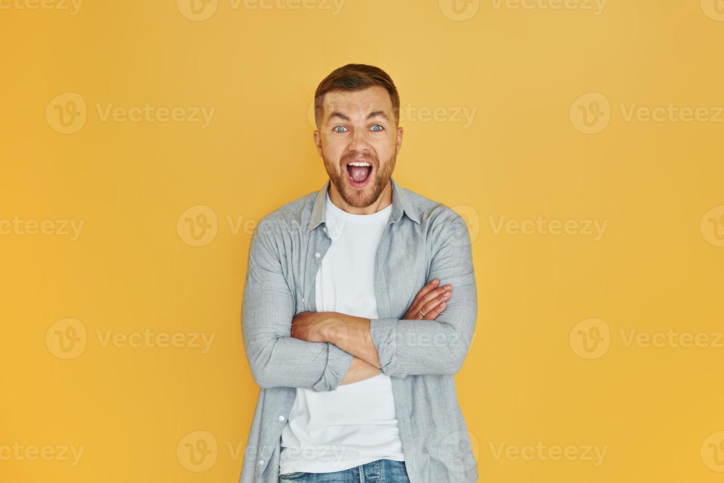 Junger Mann in Freizeitkleidung, der drinnen im Studio vor orangefarbenem Hintergrund steht foto