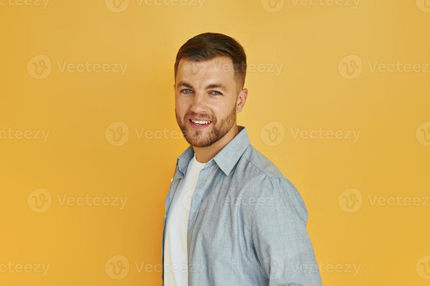 Junger Mann in Freizeitkleidung, der drinnen im Studio vor orangefarbenem Hintergrund steht foto