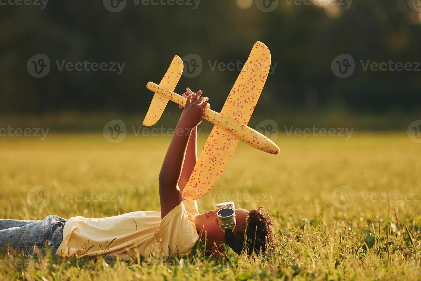 mit Spielzeugflugzeug auf dem Rasen niederlegen. afroamerikanisches kind hat tagsüber im sommer spaß auf dem feld foto