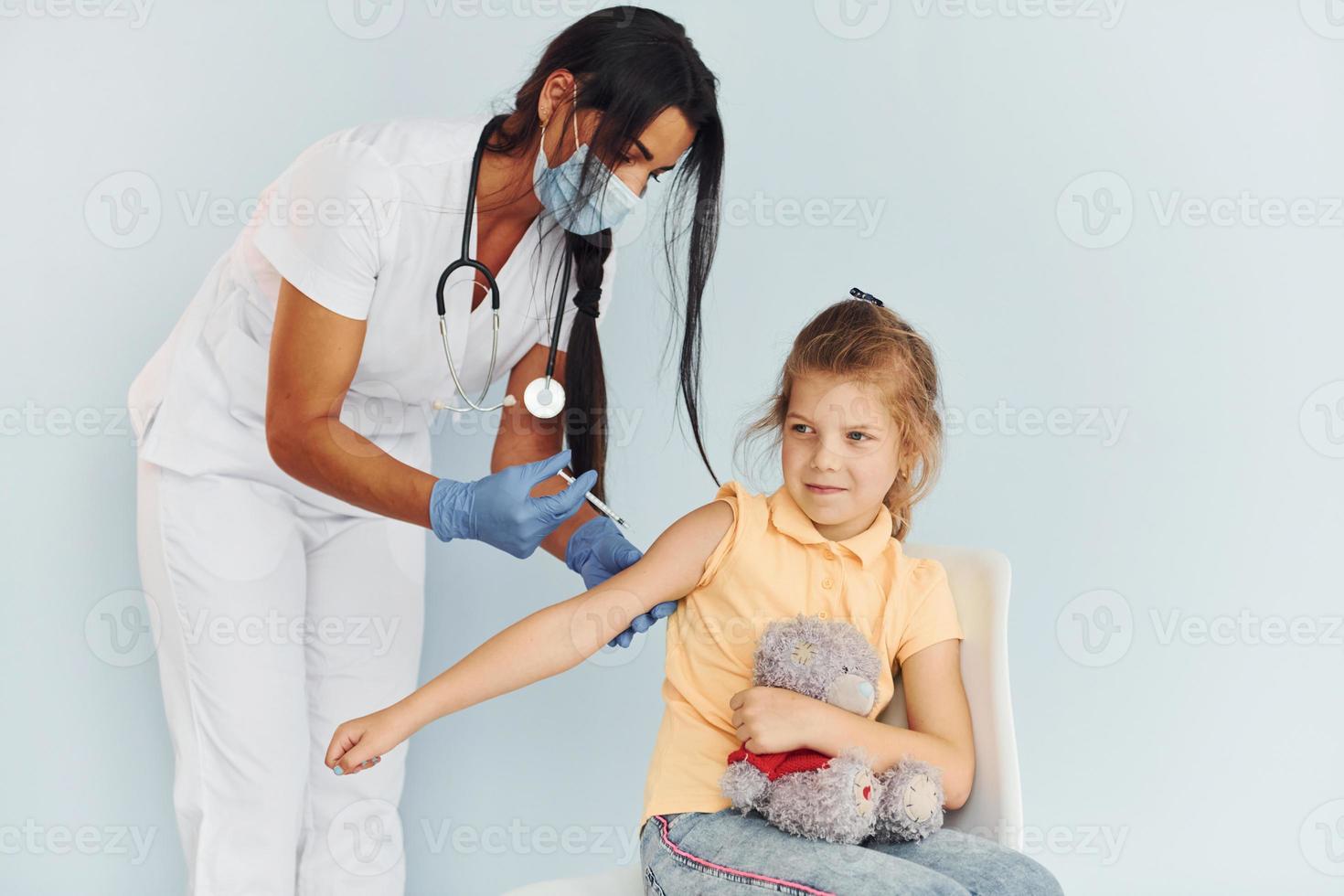kleines Mädchen mit Teddybär. Arzt in Uniform, der dem Patienten eine Impfung vornimmt foto