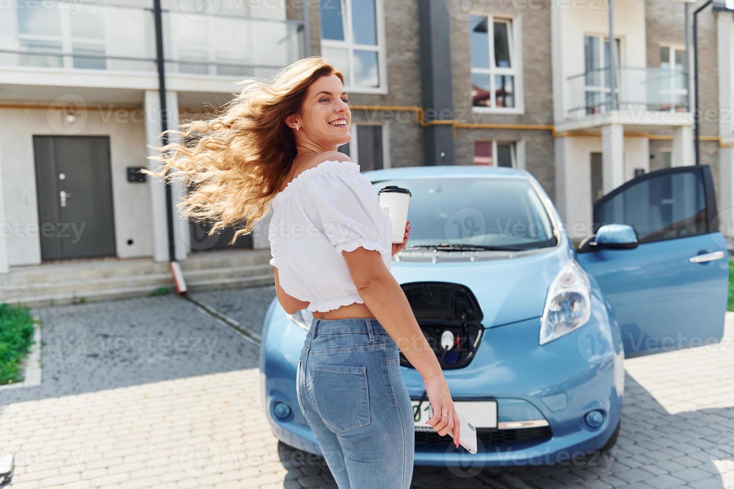 mit Trinkbecher. Junge Frau in Freizeitkleidung mit ihrem Elektromobil tagsüber im Freien foto