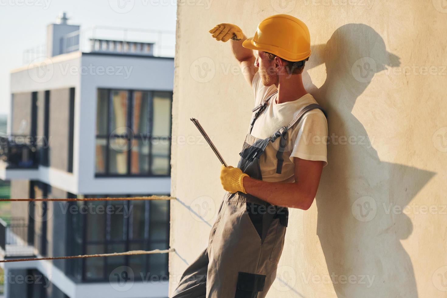 hoch oben stehen. junger mann, der tagsüber in uniform auf dem bau arbeitet foto