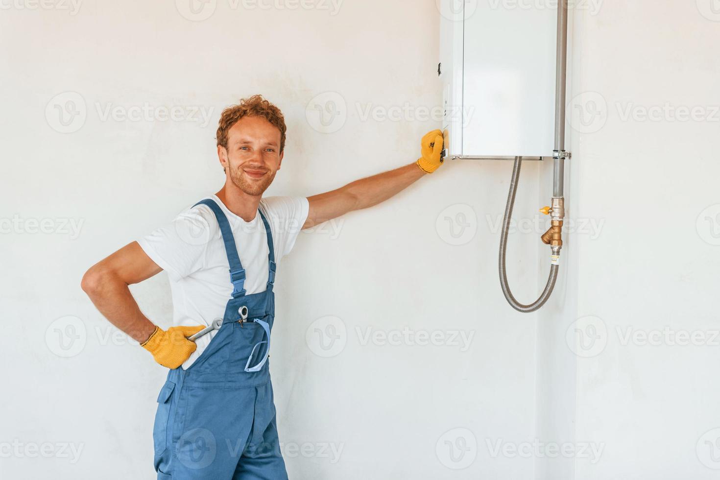 Warmwasserbereiter reparieren. junger mann, der tagsüber in uniform auf dem bau arbeitet foto