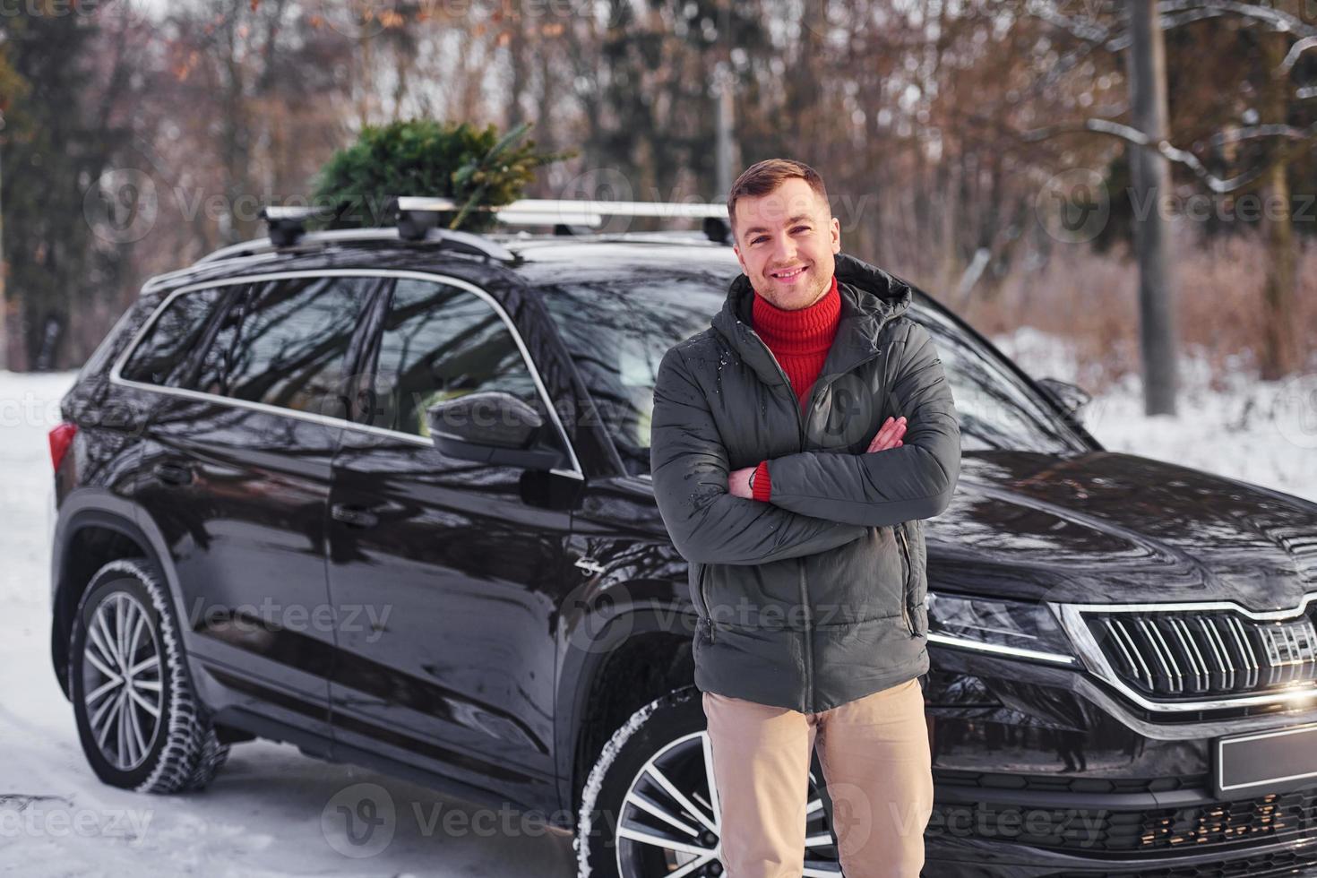 Vorderansicht. mann mit kleiner grüner tanne ist draußen in der nähe seines autos. Konzeption von Feiertagen foto