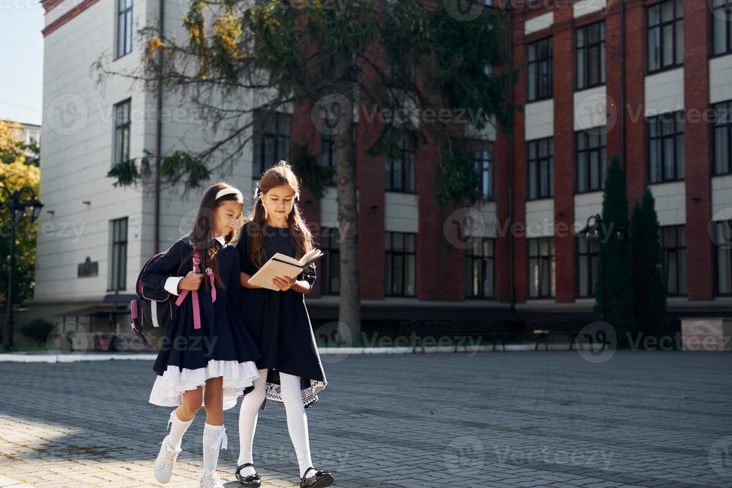 mit Büchern. Zwei Schulmädchen sind draußen zusammen in der Nähe des Schulgebäudes foto